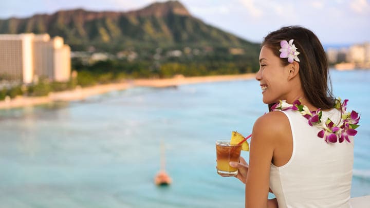 Woman drinking a Mai Tai overlooking the Diamond Head crater and Waikiki Beach