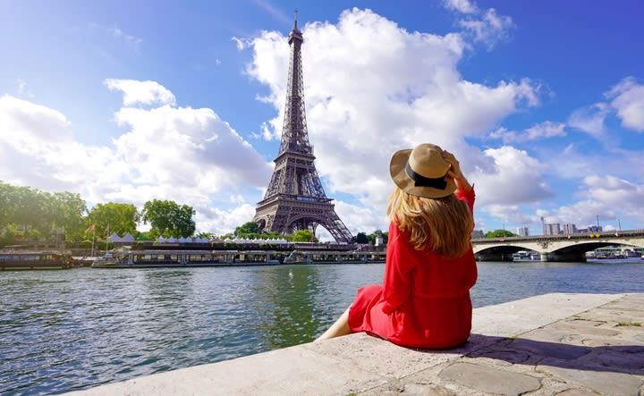 Mujer sentada a orilla del Sena mirando la Torre Eiffel, París. Qué hacer en París en las Olimpiadas.