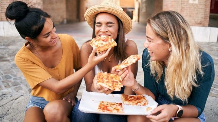 Friends eating pizza on a piazza in Rome