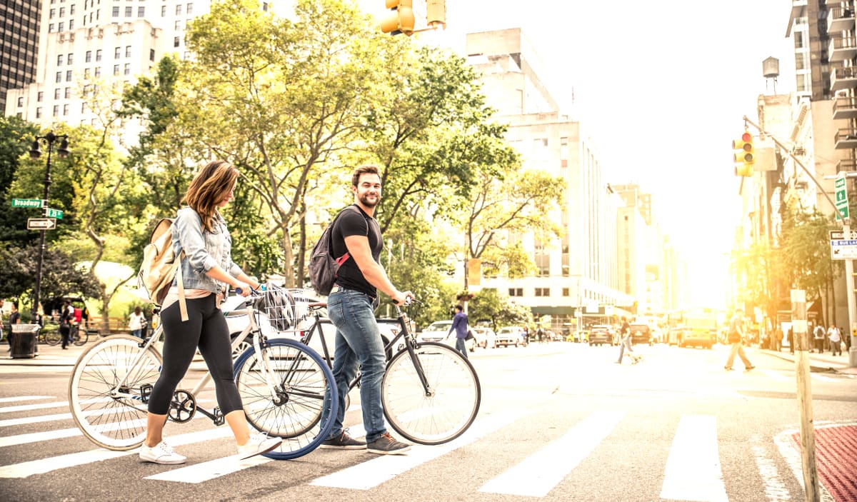 Image of Adult, Female, Person, Woman, Male, Man, Bicycle, Vehicle, Traffic Light, Car, Road, Neighborhood, City, Backpack, Bag, Pedestrian, 