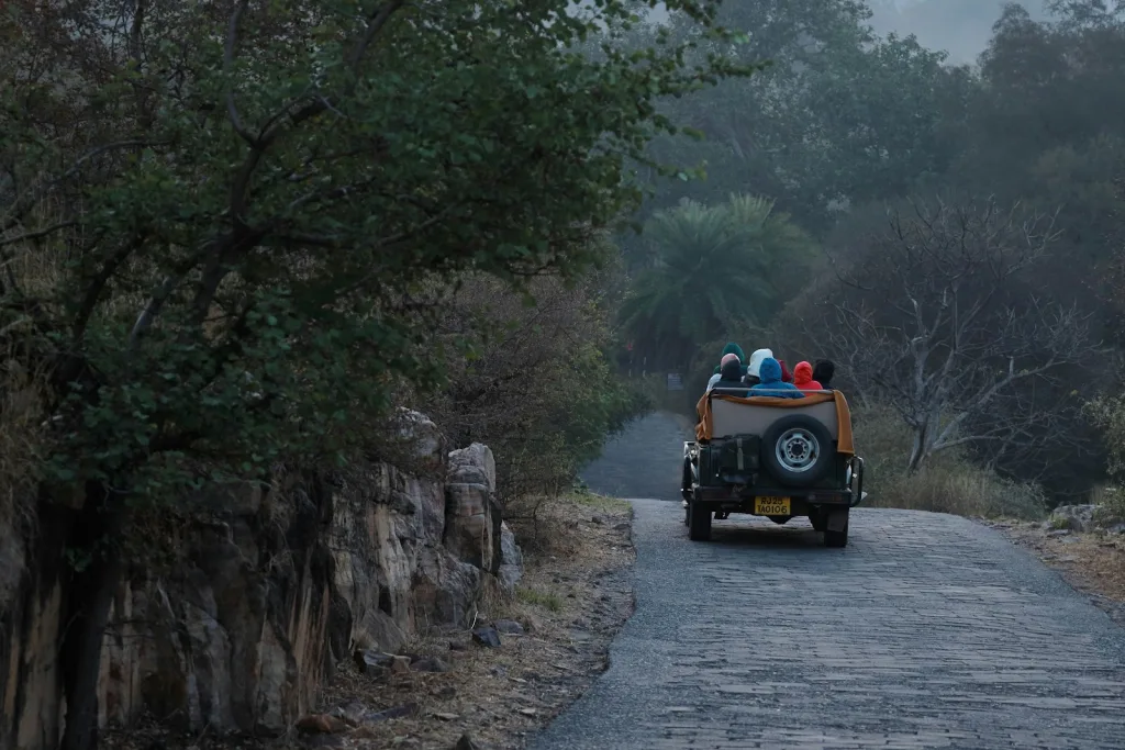 Open safari gypsy with passengers in warm hooded jackets on a forest road in Ranthambore