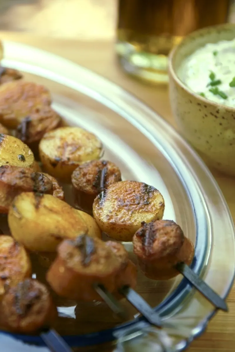 Assiette présentant des brochettes de saucisses et de pommes de terre accompagnée d'un bol avec une sauce ranch