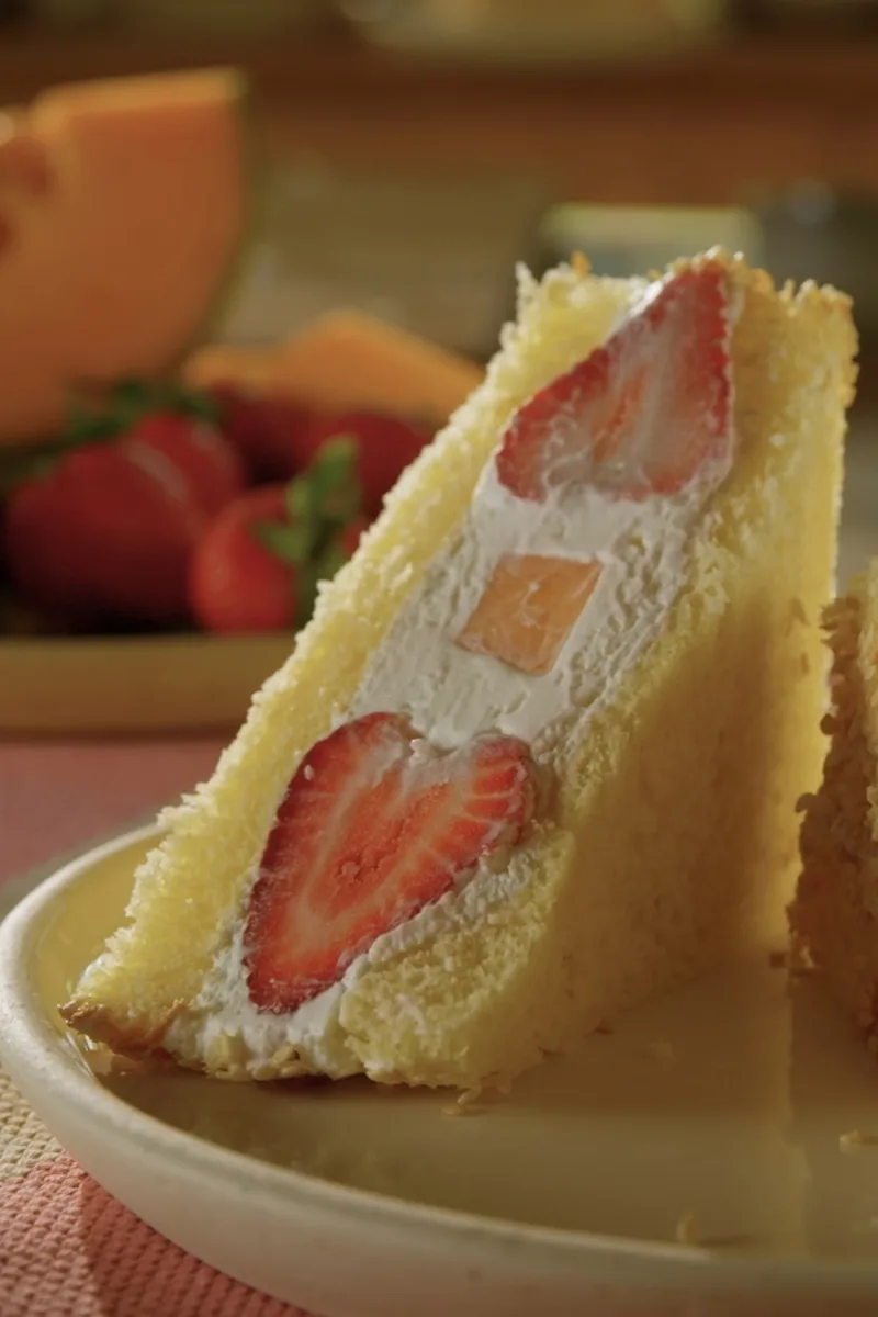 Deux quartiers d'un sandwich dessert aux fraises et au cantaloup servis dans une assiette, à côté de cantaloup et de fraises frais
