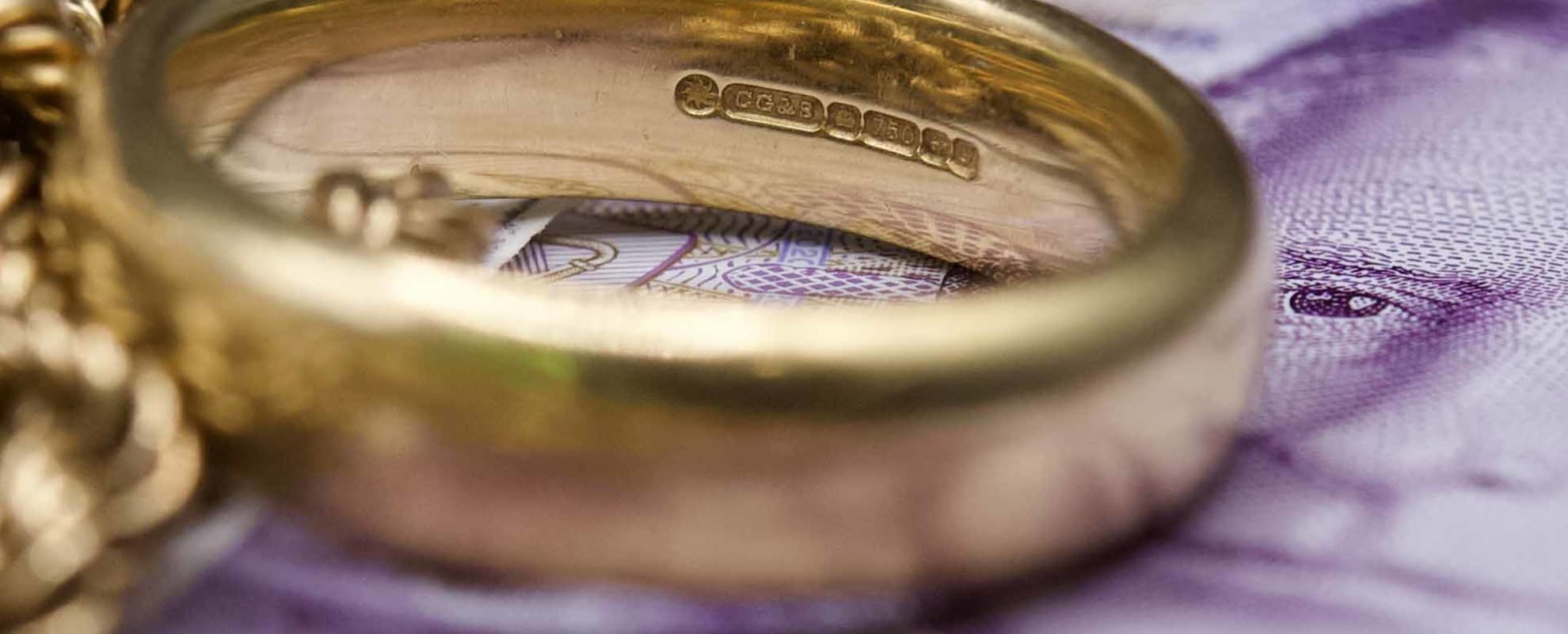 A pile of scrap gold, sitting on top of a bundle of £20 notes, with focus on an 18 carat wedding band