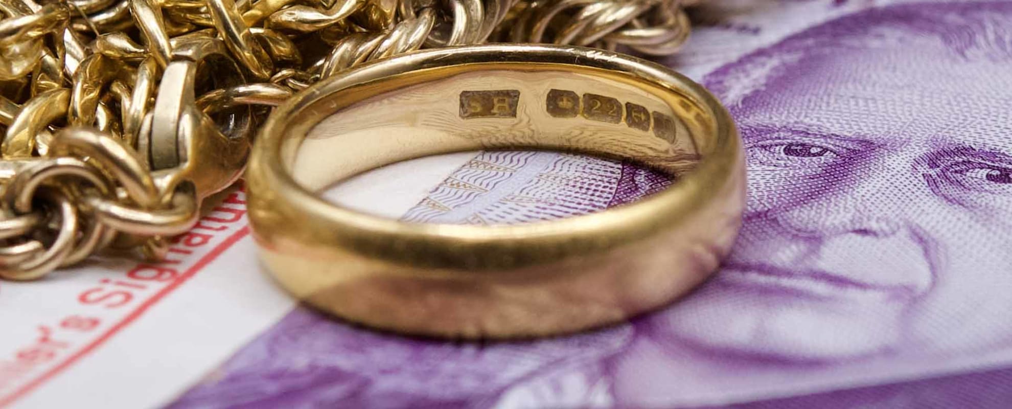 A pile of scrap gold, sitting on top of a bundle of £20 notes, with focus on a 22ct hallmark