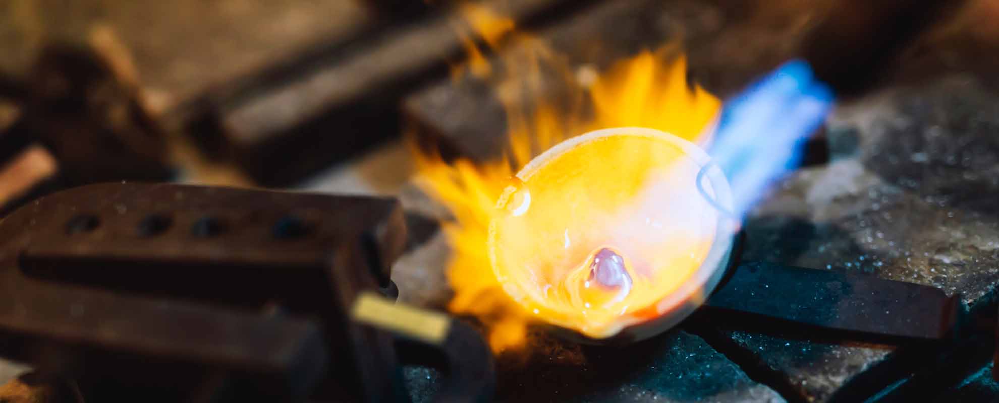 A button on molten gold in a ceramic crucible, being heated with a blowtorch