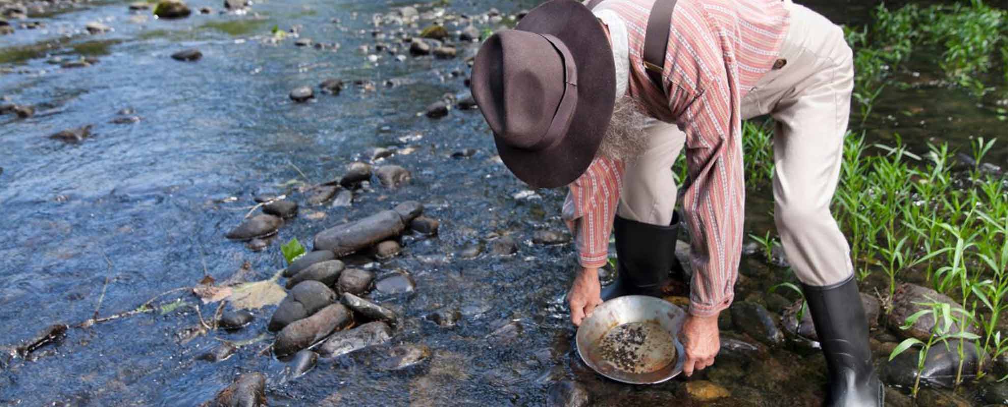 An elderly man, stood in a river, panning for gold