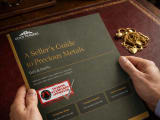 A hand model, holding a printed copy of our Sellers Guide to Precious Metals, with a pile of scrap gold on a desk