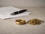 A small quantity of gold jewellery in the foreground, with a formal looking letter, blurred out, in the background