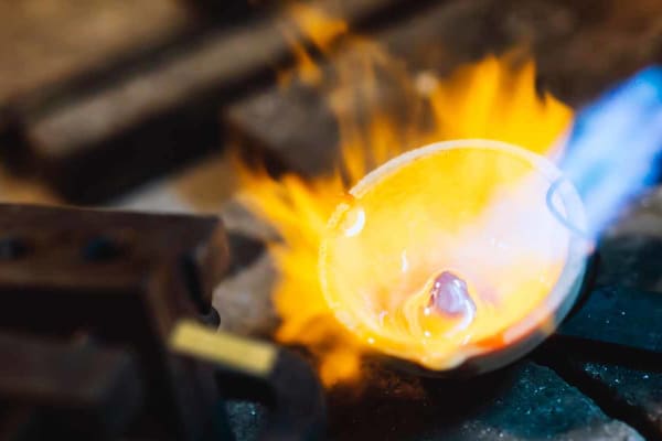 A button on molten gold in a ceramic crucible, being heated with a blowtorch