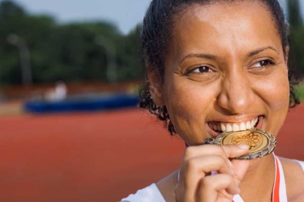 A female athlete with a medal round her neck, which she is 'biting'