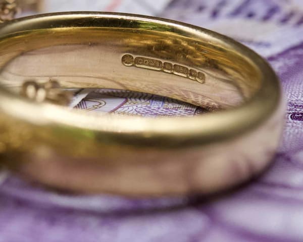 A pile of scrap gold, sitting on top of a bundle of £20 notes, with focus on an 18 carat wedding band