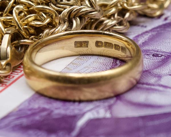 A pile of scrap gold, sitting on top of a bundle of £20 notes, with focus on a 22ct hallmark