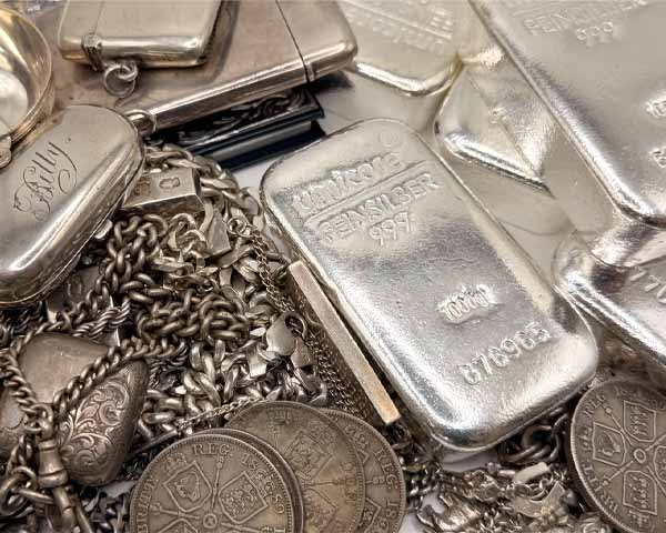 A pile of scrap silver next to 1kg silver bars