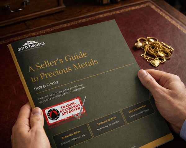 A hand model, holding a printed copy of our Sellers Guide to Precious Metals, with a pile of scrap gold on a desk