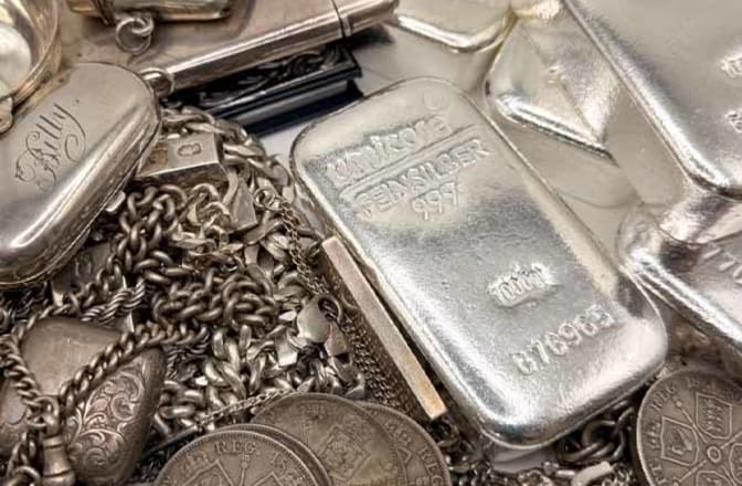 A pile of scrap silver next to 1kg silver bars