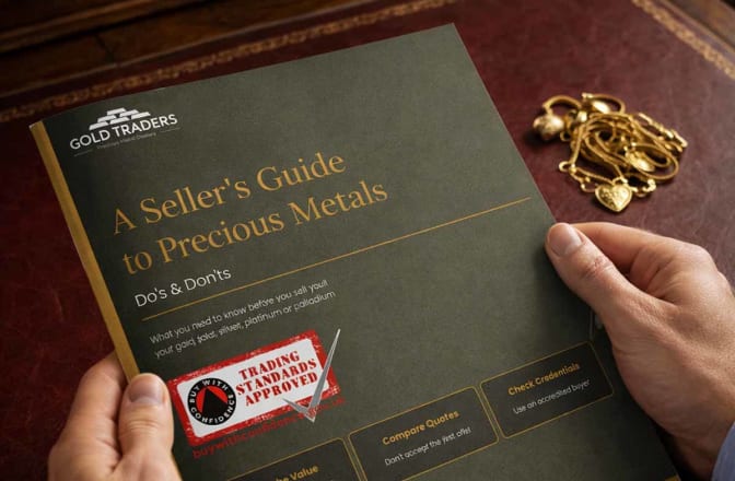 A hand model, holding a printed copy of our Sellers Guide to Precious Metals, with a pile of scrap gold on a desk