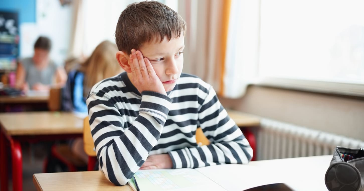 Bored little school boy in classroom looking out of window
