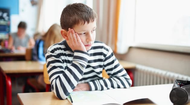 Bored little school boy in classroom looking out of window
