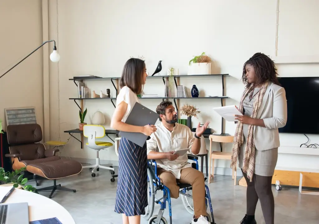 Image of 3 people working, two of them are women and one is a man who is in a wheelchair.