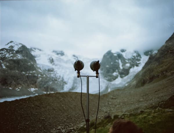 Video still showing a microphone that is directed towards a blurry glacier in the background.