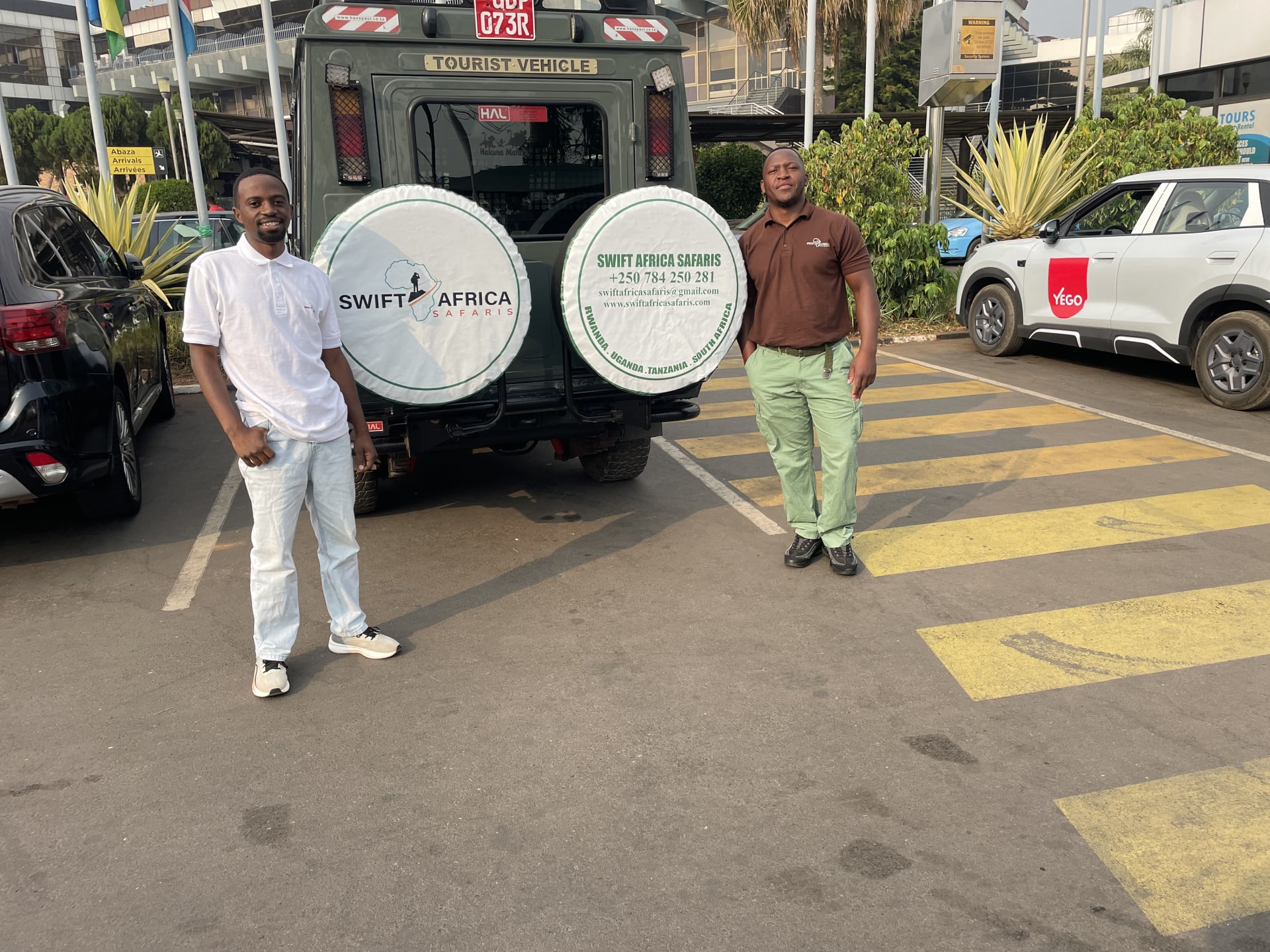 A Swift Africa Safaris vehicle and two team members in a car park in Rwanda