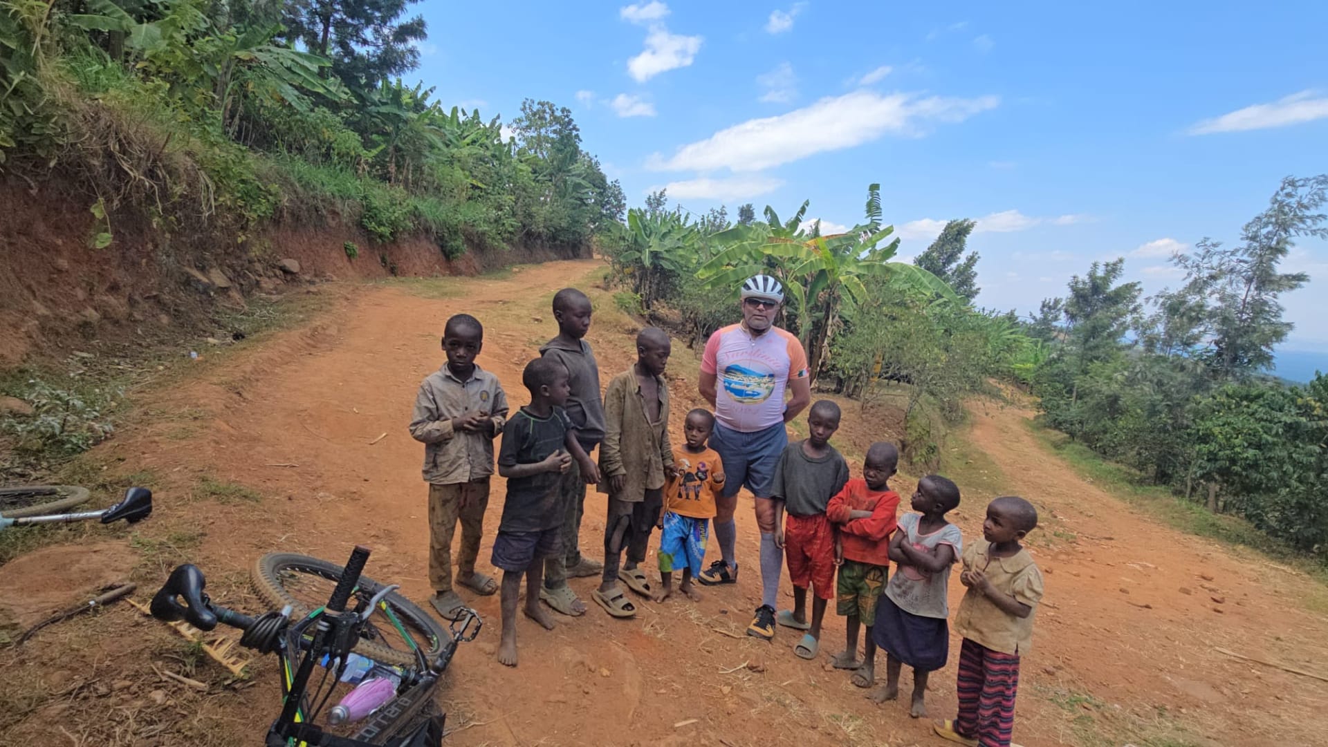 Children and a traveller with a bicycle on a red dirt road in a village on the Congo Nile Trail