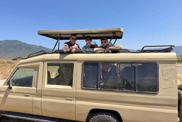 A safari vehicle with a pop-up roof and guests on a game drive in East Africa
