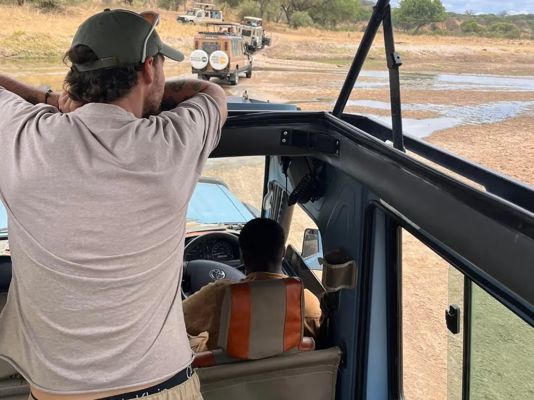 Un homme debout dans un véhicule safari ouvert regardant une rivière avec d'autres véhicules derrière.