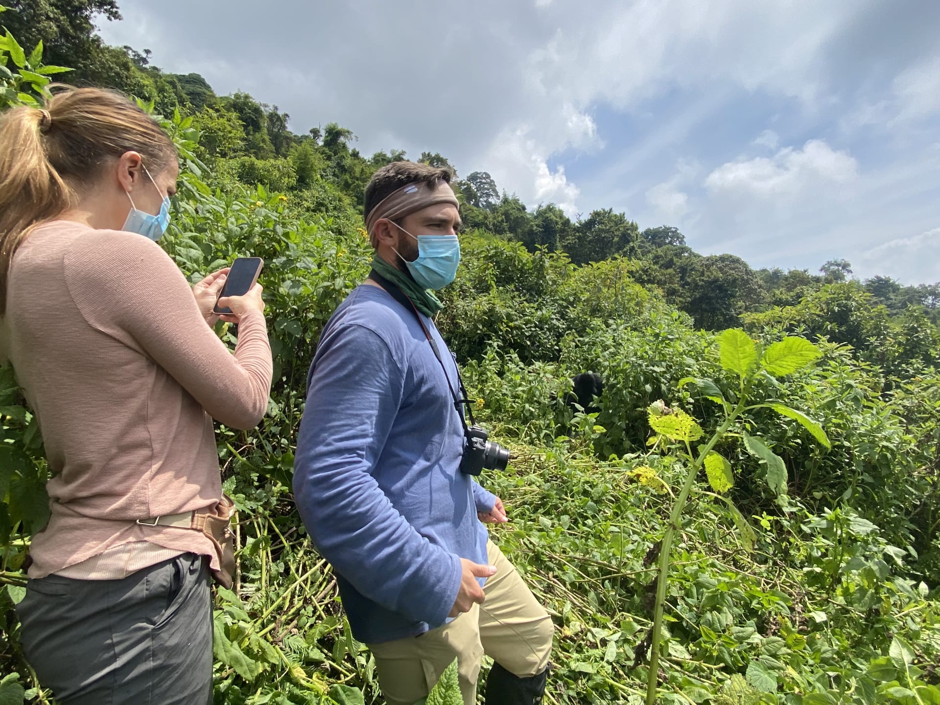 Two trekkers wearing face masks on a hillside in Mgahinga Gorilla National Park