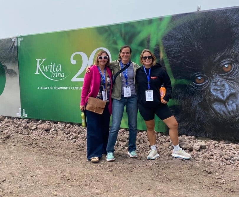 Tres mujeres vestidas con atuendo tradicional vibrante asistiendo a la celebración Kwita Izina, mostrando la belleza y la unidad de la cultura Rwanda
