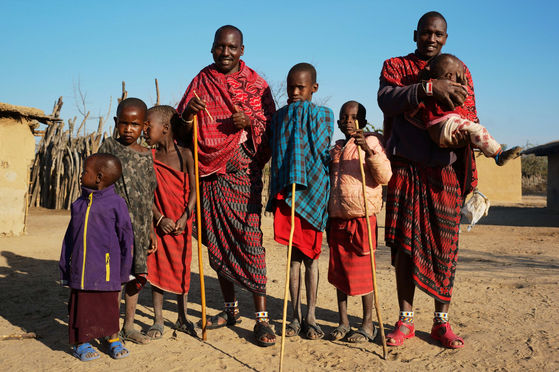Ein Maasai-Mann trägt ein Kind mit anderen Kindern und Männern in einem Dorf