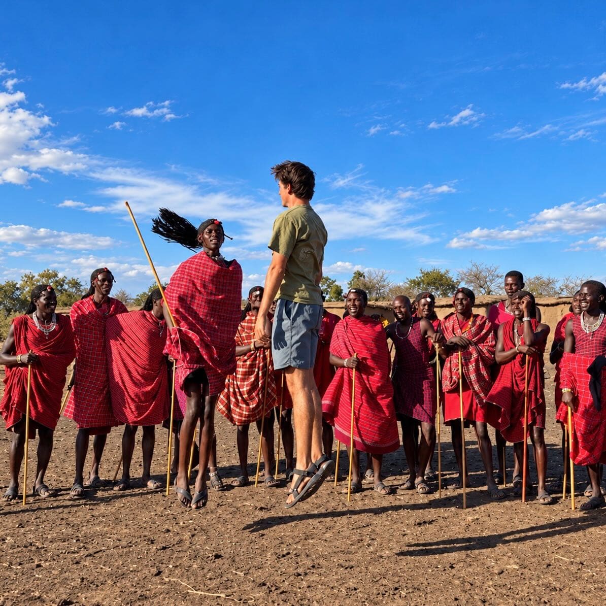 Maasai men in red shukas lined up in front of a guest in a village