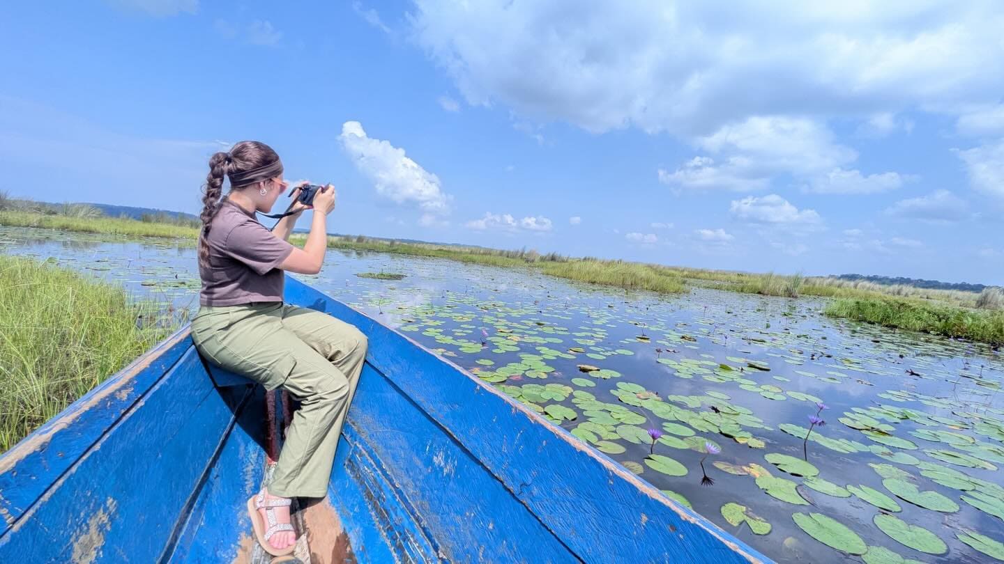 A visitor in a blue canoe photographing among water lilies at Mabamba Swamp