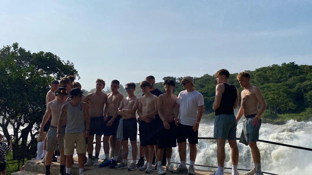 Cette photo capture un groupe joyeux de touristes masculins se tenant ensemble lors d'une aventure inoubliable pendant Uganda Safaris for Families: Wildlife and Culture Tours, alors qu'ils prennent des photos incroyables de la beauté naturelle environnante. Les voyageurs sourient, sont détendus et profondément engagés, tenant des appareils photo et des smartphones tout en documentant un moment partagé dans les paysages à couper le souffle de l'Ouganda. Derrière eux, le paysage reflète l'essence de la riche biodiversité de l'Ouganda, des savanes ouvertes et de la chaleur culturelle. L'image symbolise des expériences de safari adaptées aux familles en Ouganda, où les rencontres avec la faune se mêlent harmonieusement à l'exploration culturelle. Ces safaris offrent des voyages sûrs, éducatifs et inspirants, idéaux pour les familles à la recherche de voyages significatifs, d'une culture africaine authentique et de liens étroits avec la nature. La photographie met en avant les liens, la découverte et les souvenirs inoubliables créés grâce aux safaris en Ouganda conçus pour les familles qui apprécient la faune, la culture et l'aventure partagée.