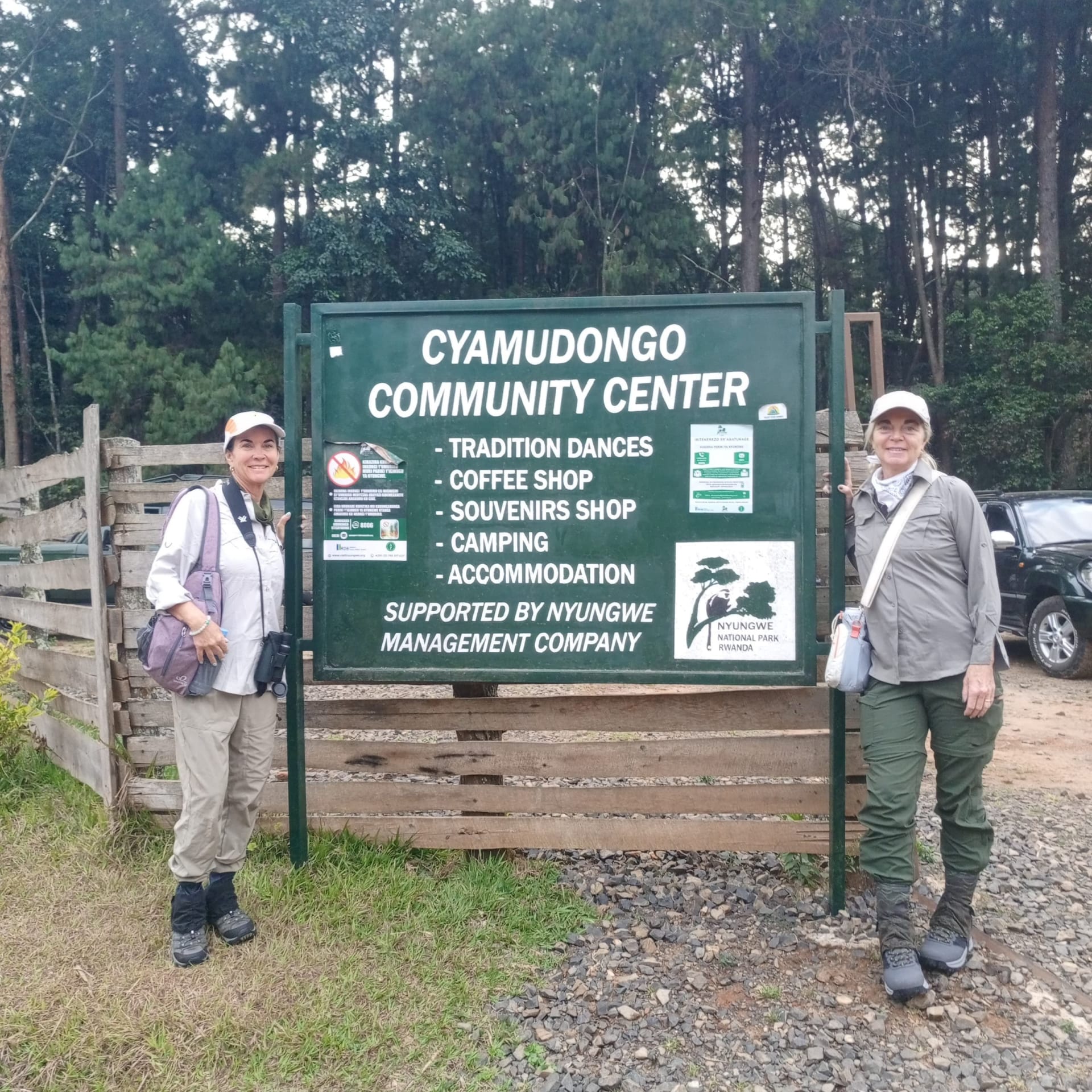 Two visitors beside the Cyamudongo community centre sign at the start of chimpanzee tracking in Rwanda