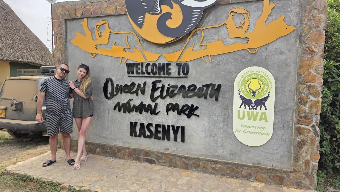 A couple beside the Kasenyi entrance sign of Queen Elizabeth National Park