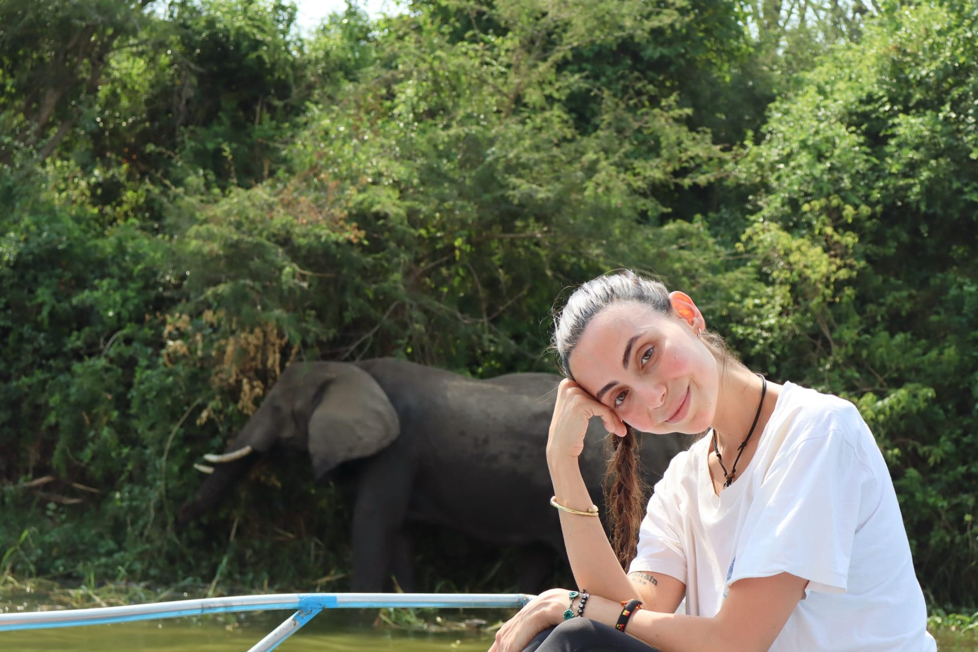 A woman resting her head on her hand with an elephant on the water edge behind her