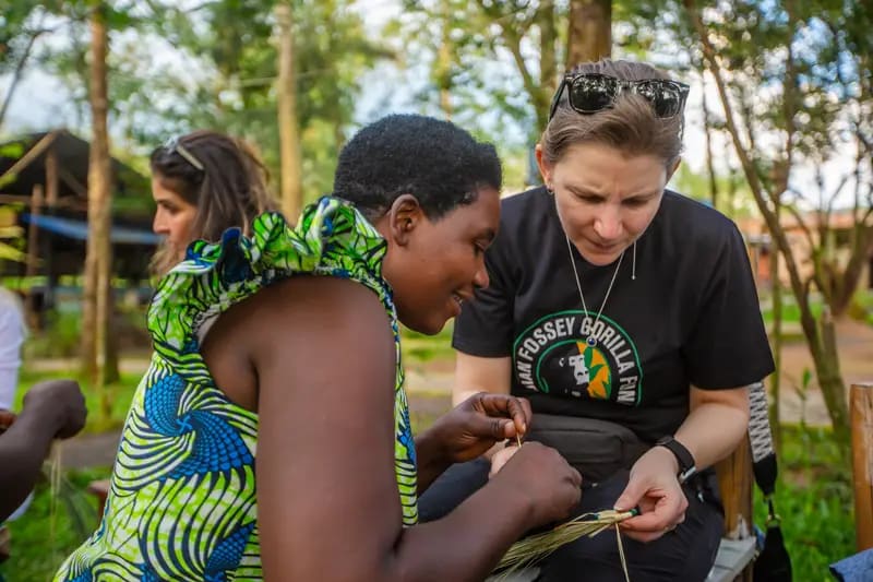 A visitor learning a craft from a Rwandan woman in a village