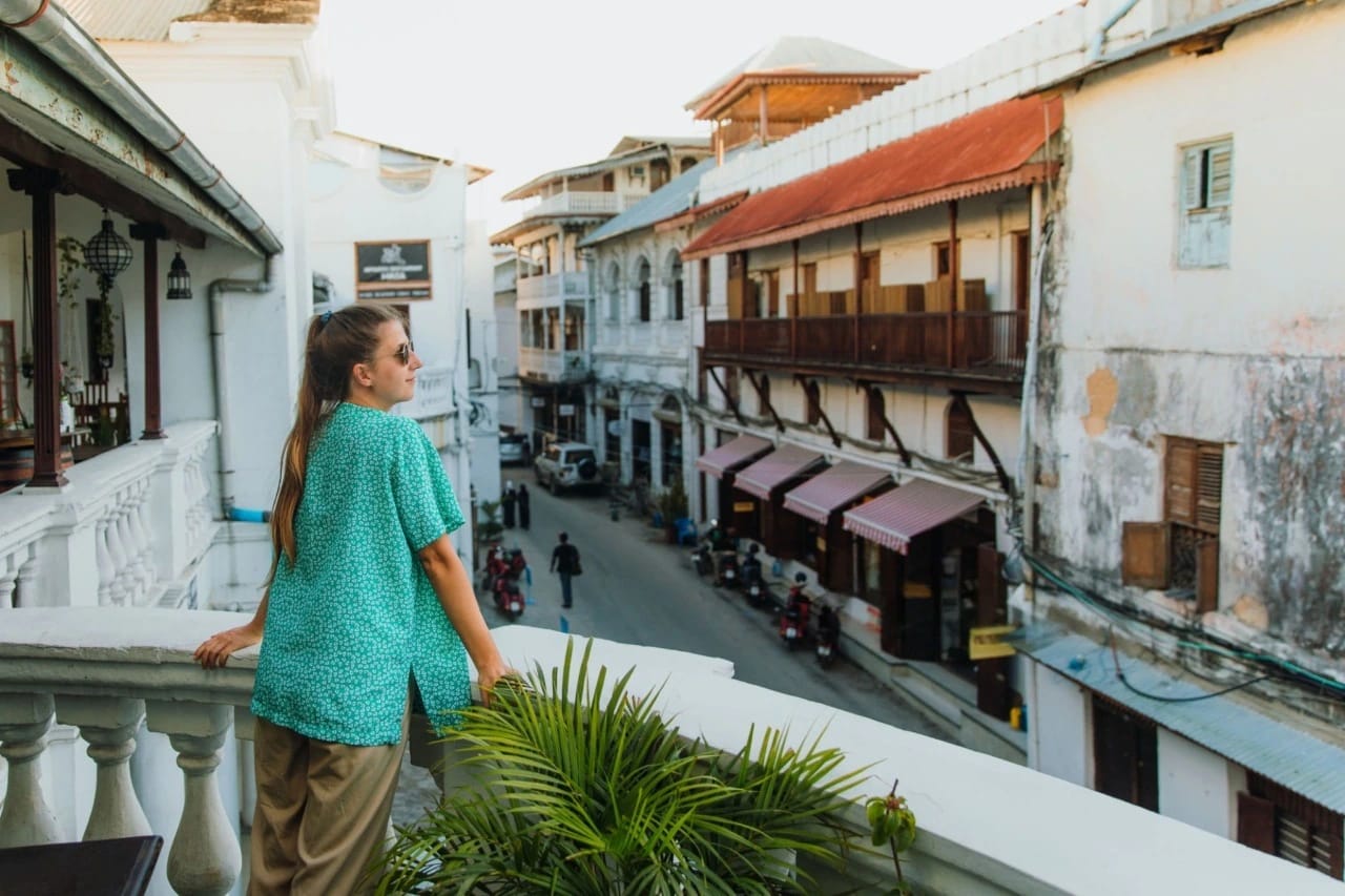 Reisender steht auf einem historischen Balkon mit Blick auf Stone Town in Zanzibar bei Sonnenuntergang — Wie man Zanzibar besucht & erlebt: Ultimativer Reiseführer.