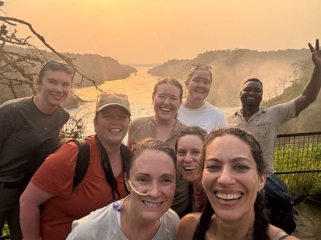 A group of smiling guests taking a selfie above Murchison Falls at sunset