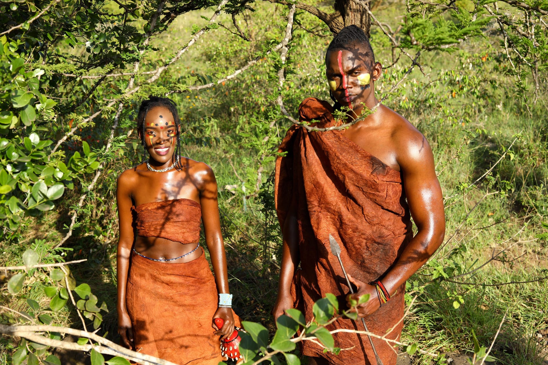 Two Batwa people in traditional dress standing among green vegetation