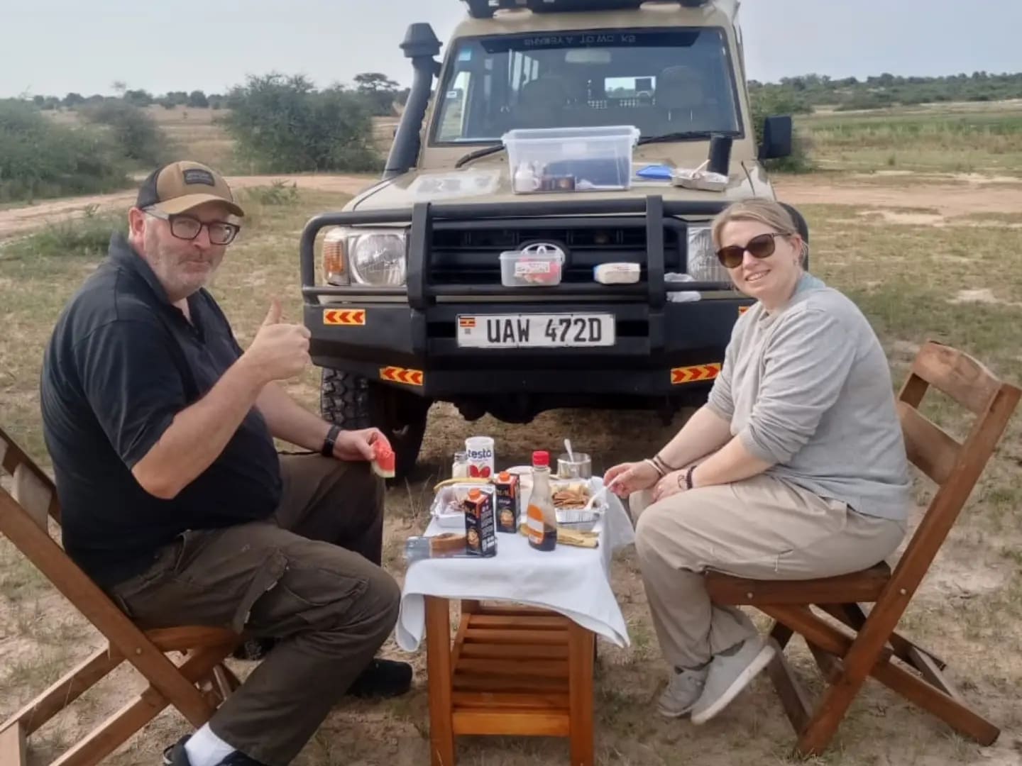 A couple having a bush breakfast beside a safari vehicle