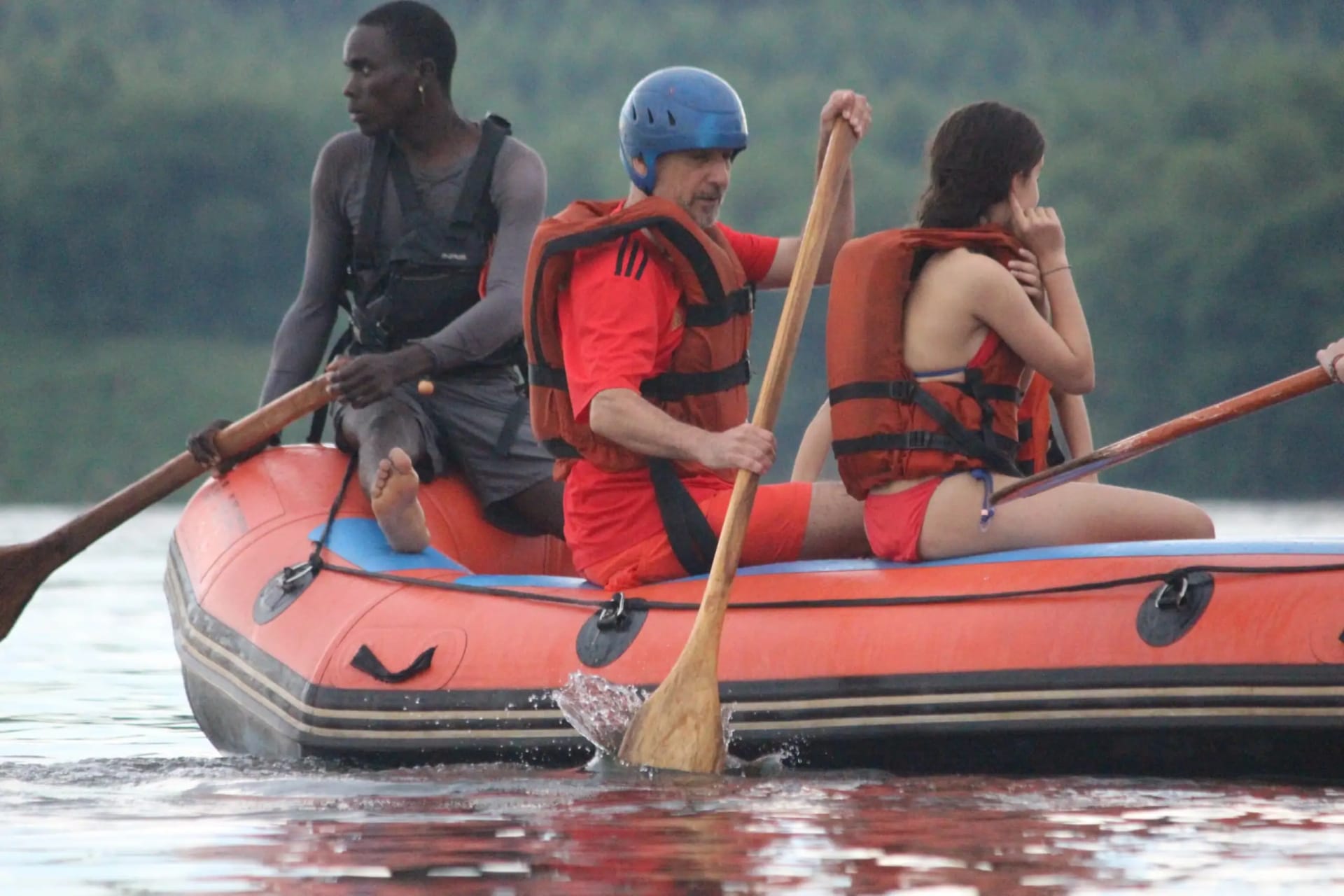 Zwei Reisende, die im Nil in Jinja, Uganda, raften, begleitet von einem lokalen Experten während einer Wildwasser-Abenteuer-Tour.
