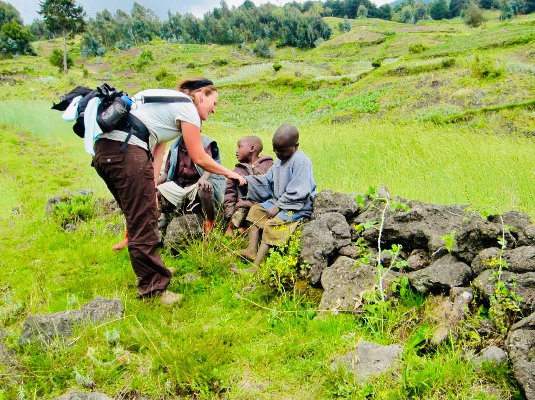 Una viajera solitaria saludando a niños locales sonrientes en un camino de pueblo, compartiendo calidez, conexión y un intercambio cultural auténtico en África