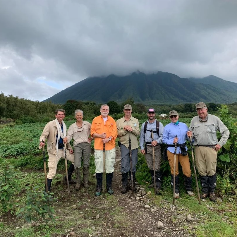 A group of trekkers and rangers on farmland below a volcano after a gorilla trek in Rwanda