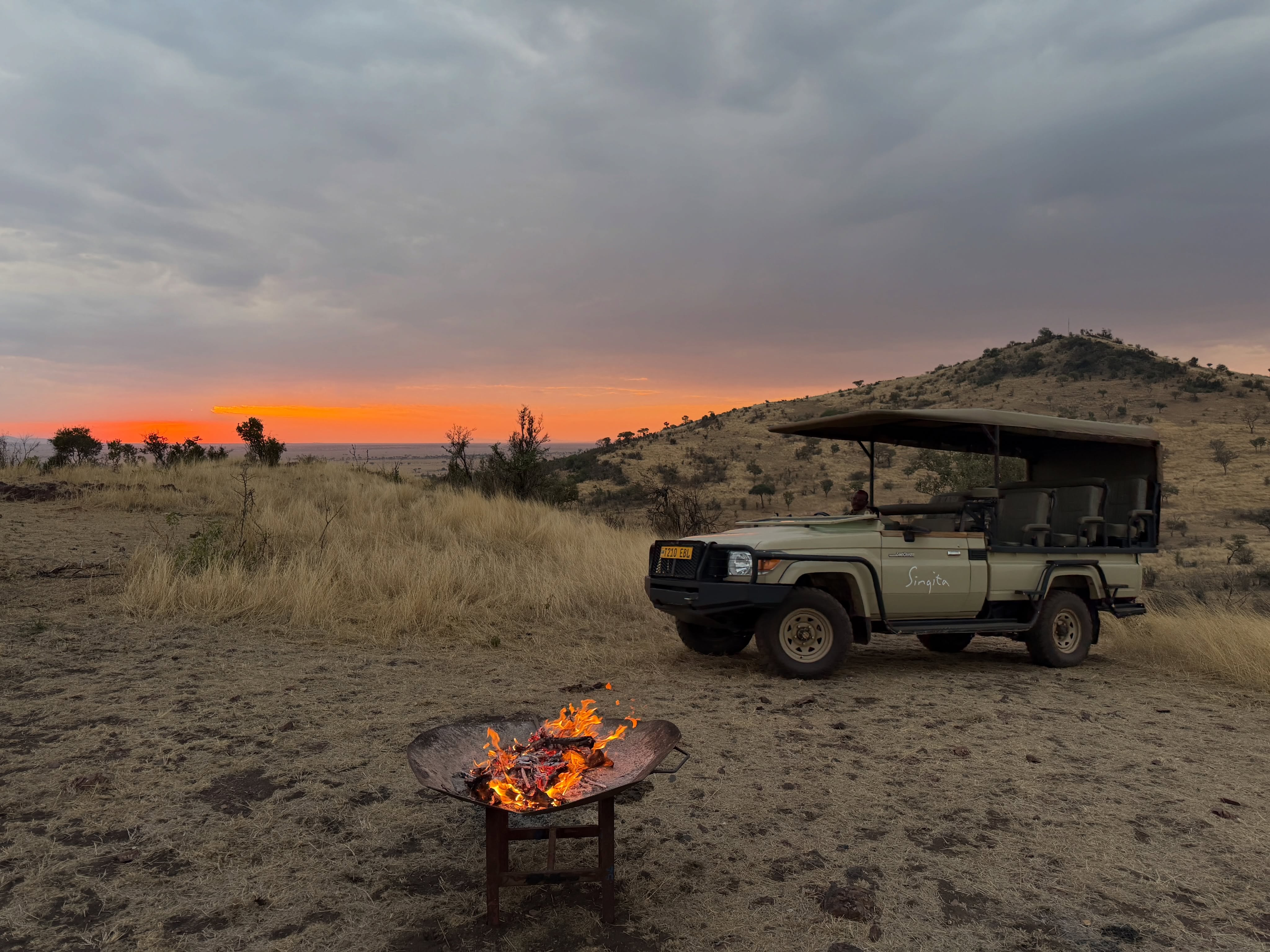 A safari vehicle and a campfire on the plains at sunset