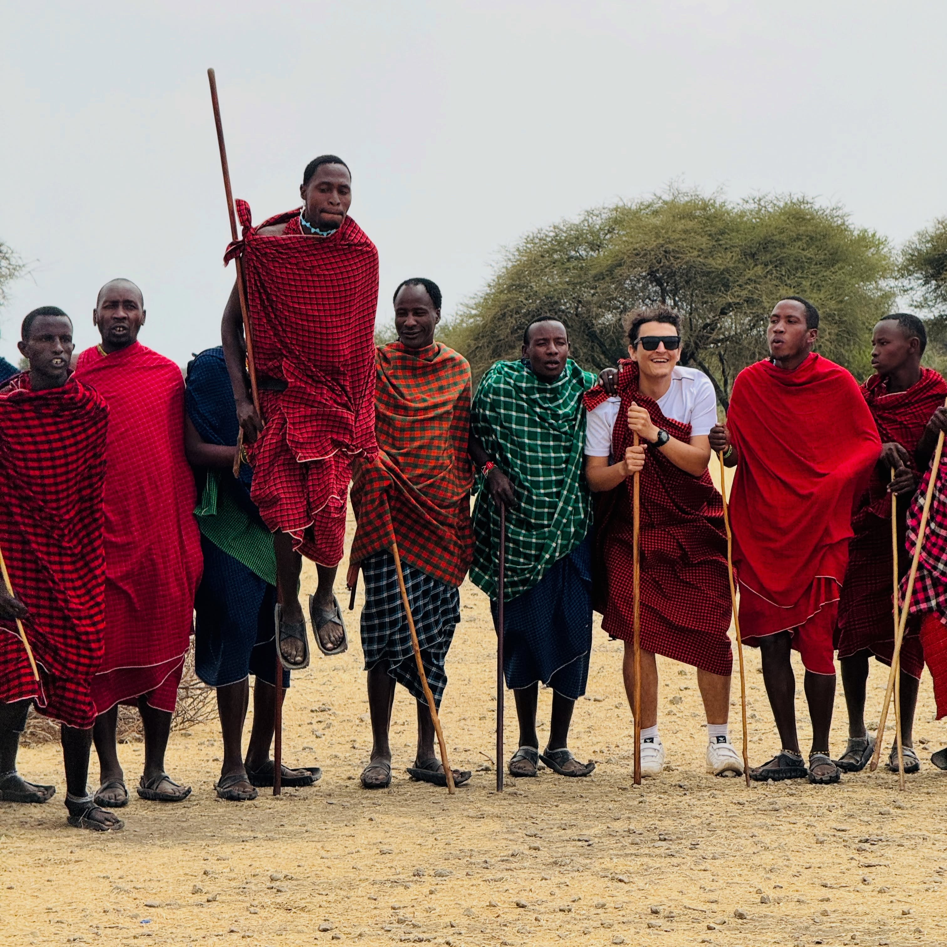 Maasai men in red cloth standing with guests in a village