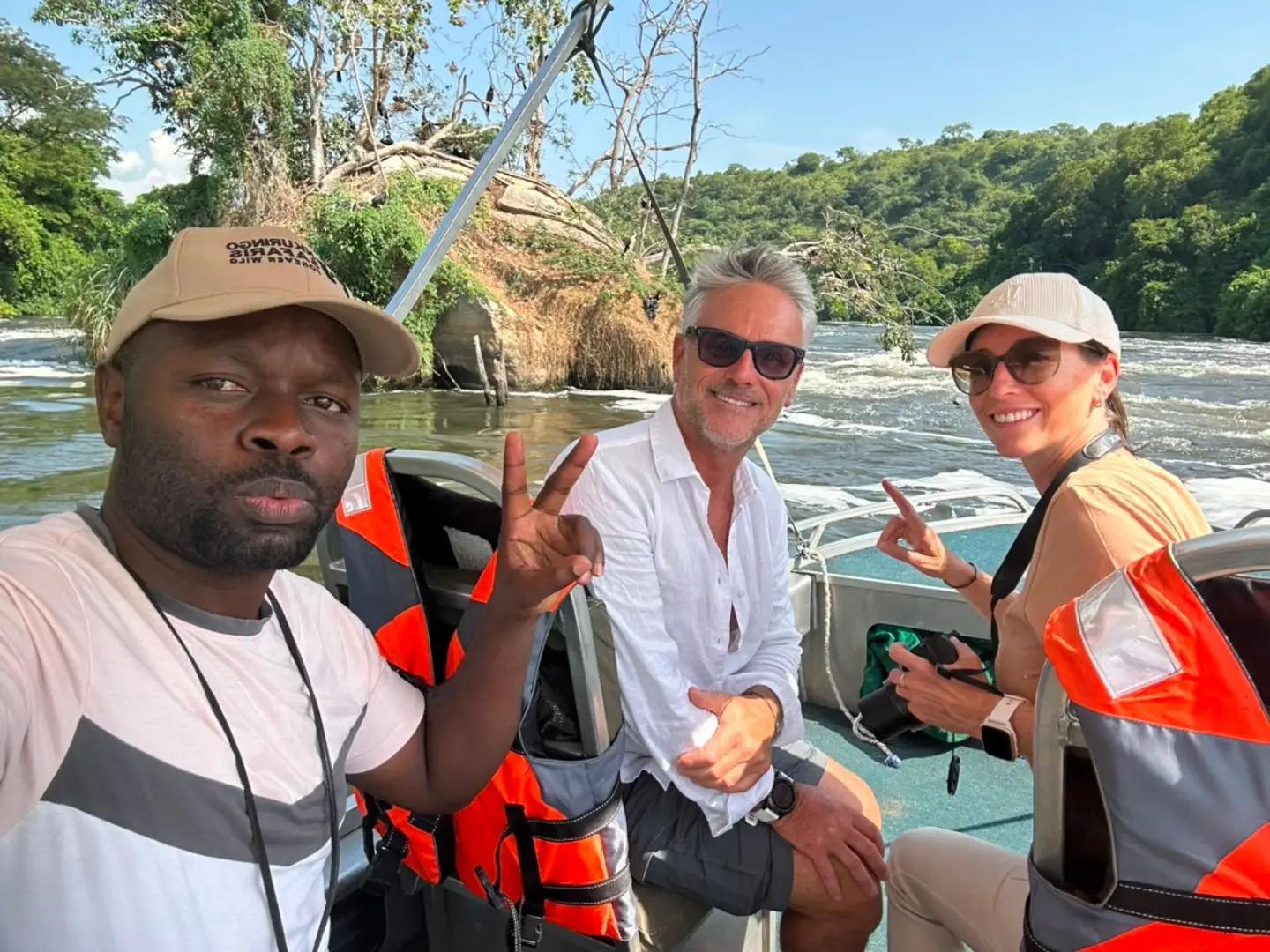 Three guests in life jackets on a boat below Murchison Falls