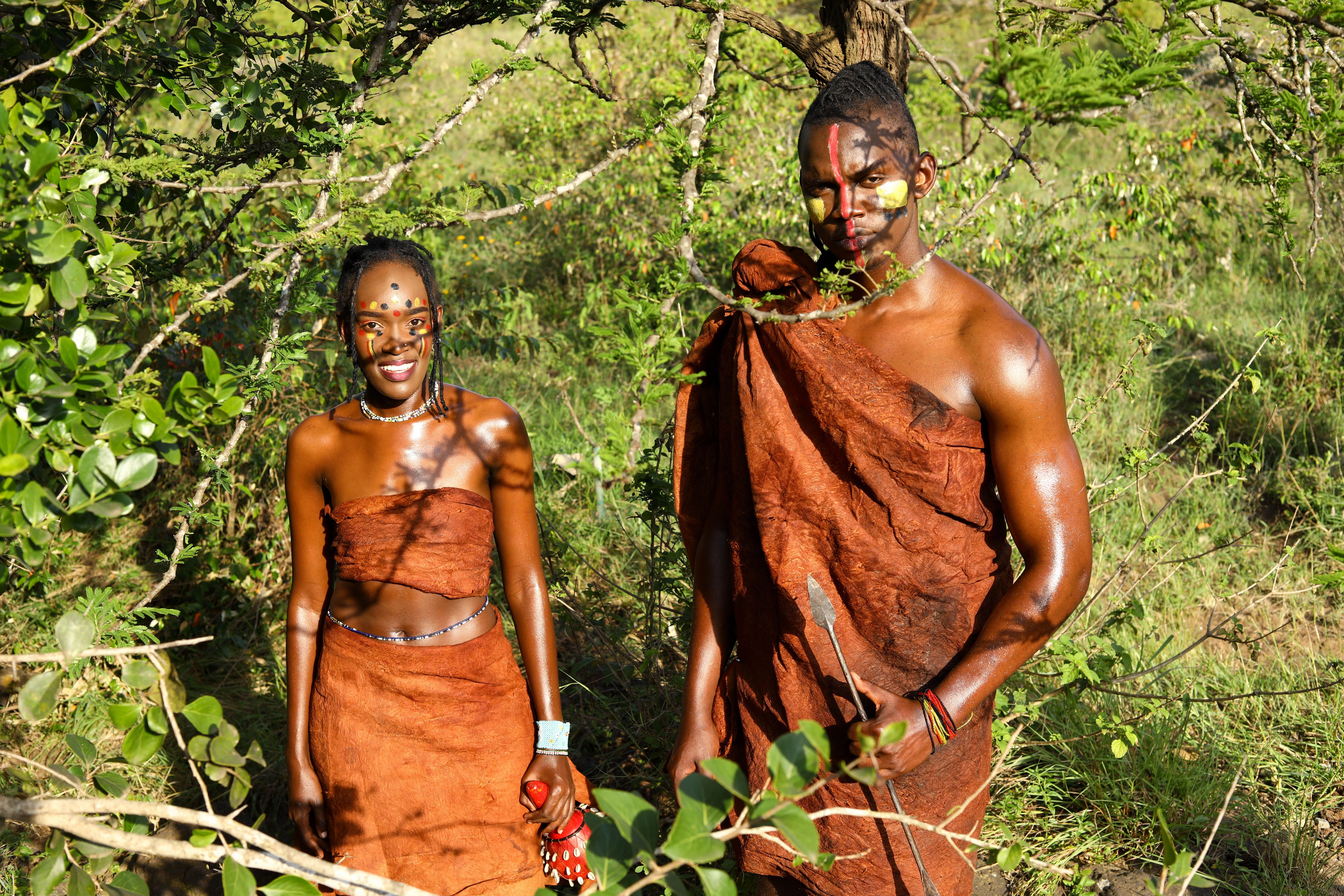 Two Batwa people in traditional dress standing among green vegetation